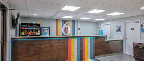 Un área de recepción con un mostrador de madera, una alfombra a rayas colorida y el número '6' grande en la pared.