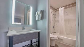 Een moderne badkamer met een witte wastafel, spiegel en douche met gordijn.