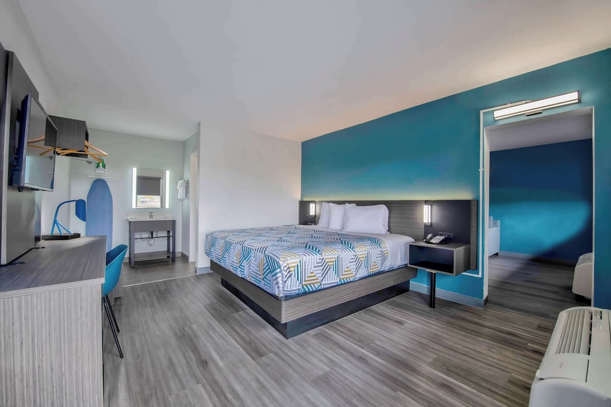 A modern hotel room with a large bed, a desk with a chair, a small bathroom, and a TV mounted on the wall.