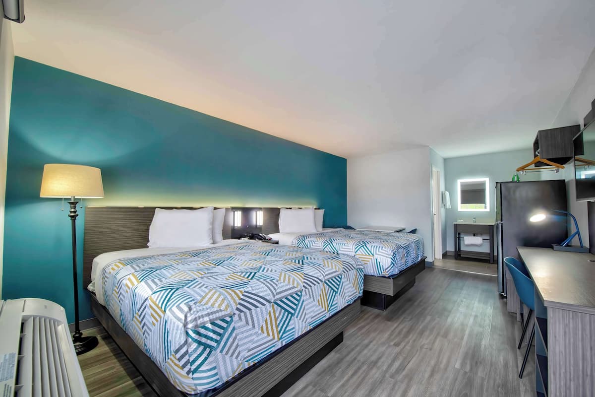 A hotel room with two beds, a desk, a mirror, and a bathroom.