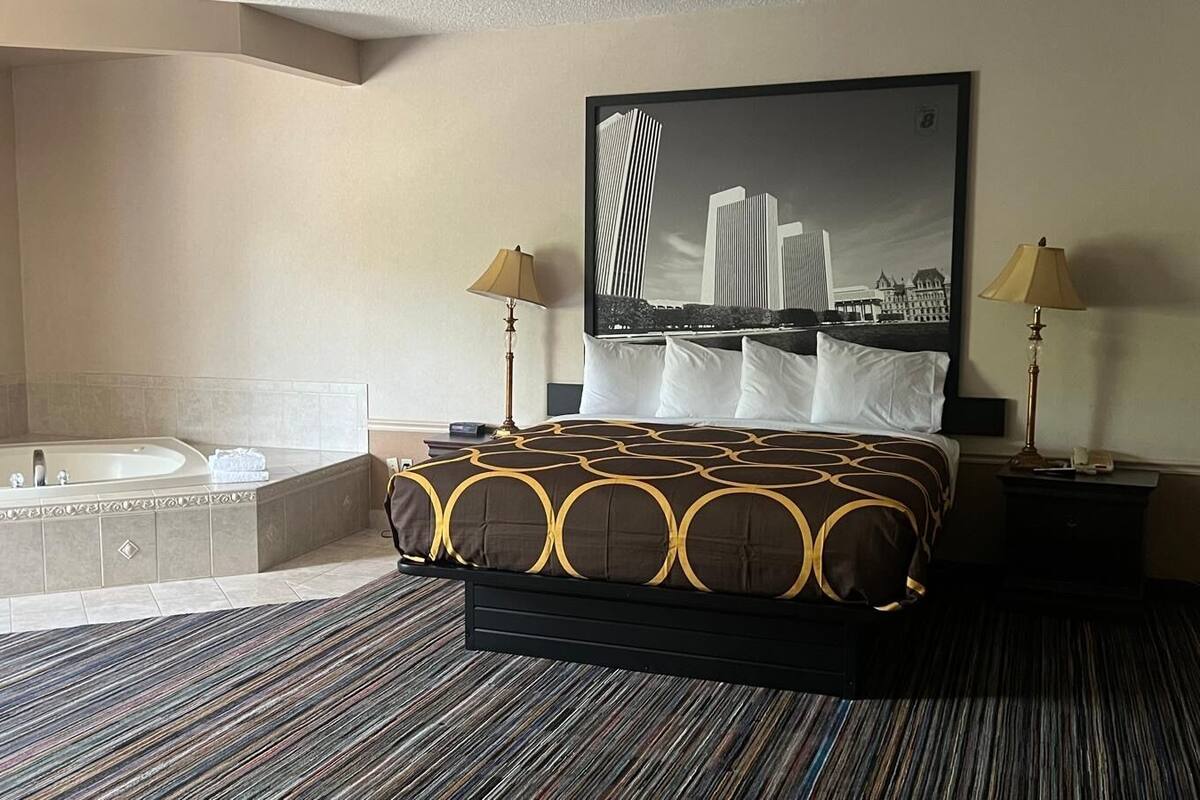 A hotel room with a large bed, a separate bathtub, two bedside lamps, and a cityscape painting on the wall.
