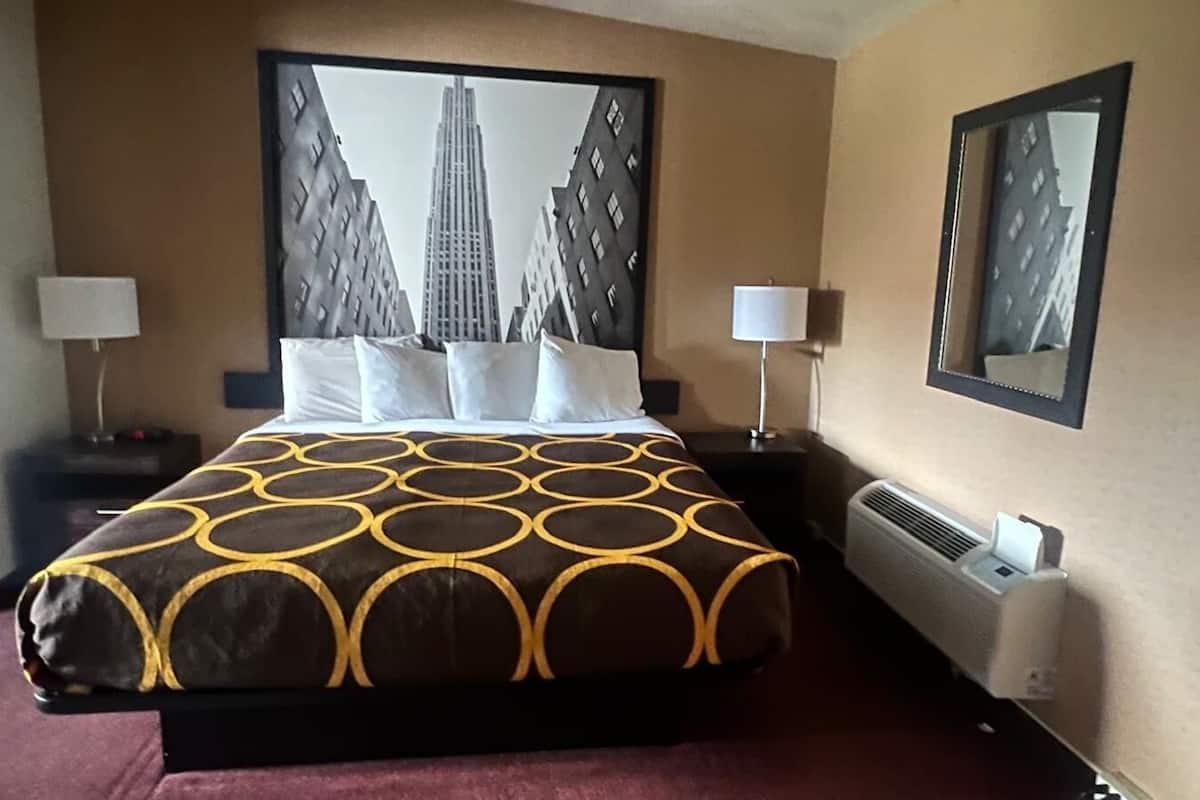 A hotel room with a large bed, two bedside tables, a wall-mounted air conditioner, and framed pictures on the walls.