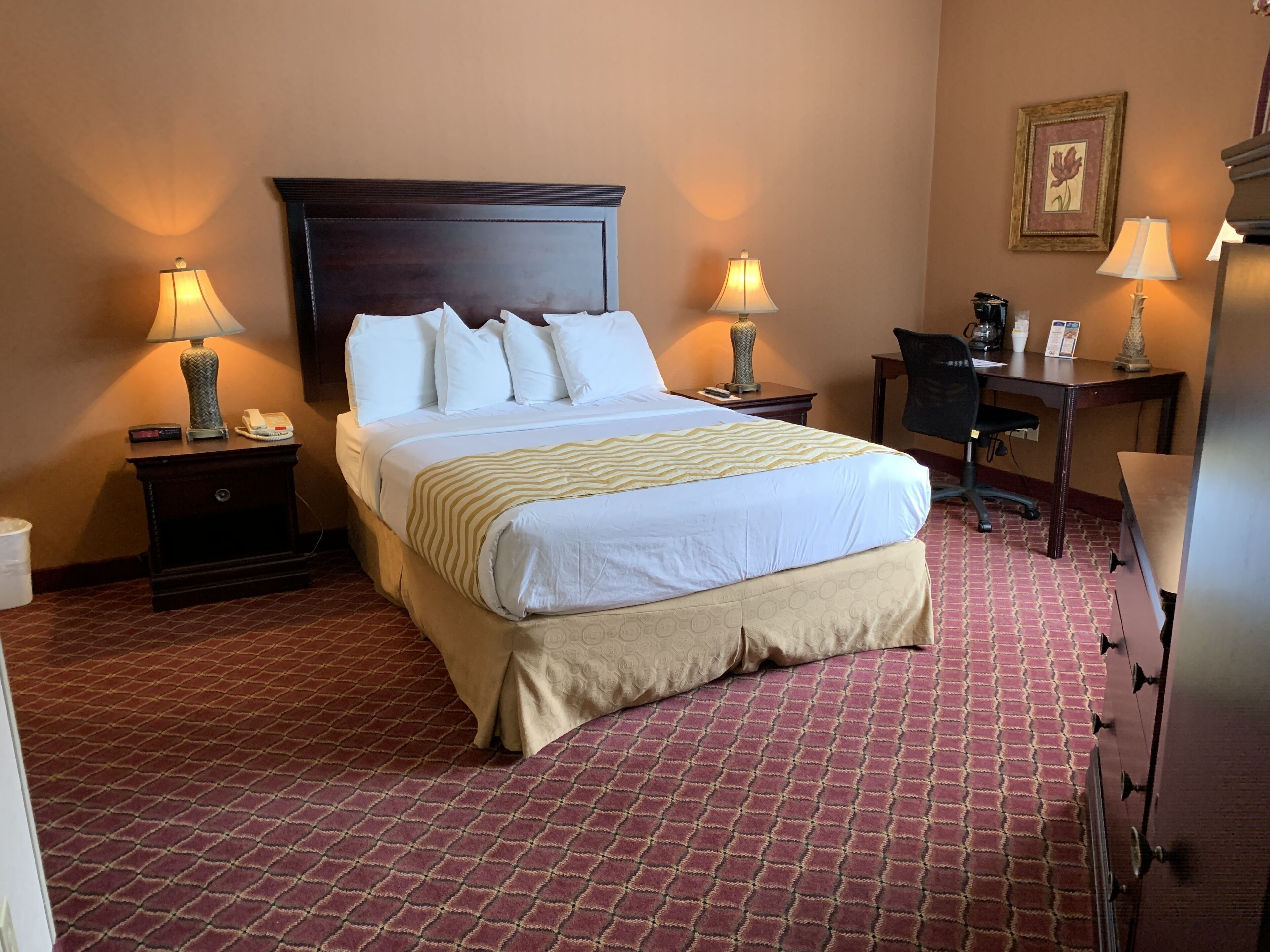 Habitación de hotel con una cama grande, dos mesitas de noche con lámparas, un escritorio con silla y un cuadro en la pared.