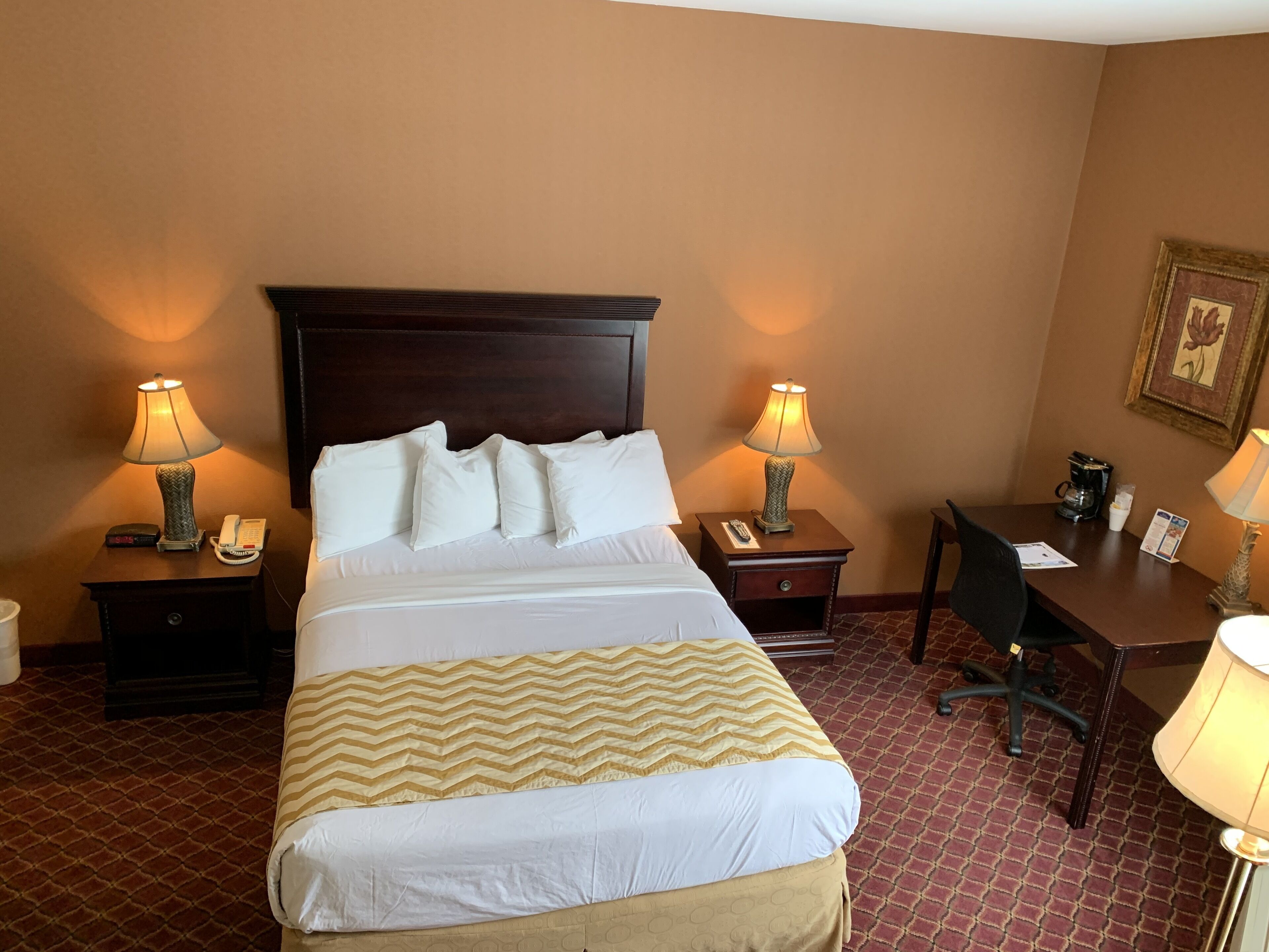 A hotel room with a large bed, two bedside tables with lamps, a desk, and a chair.