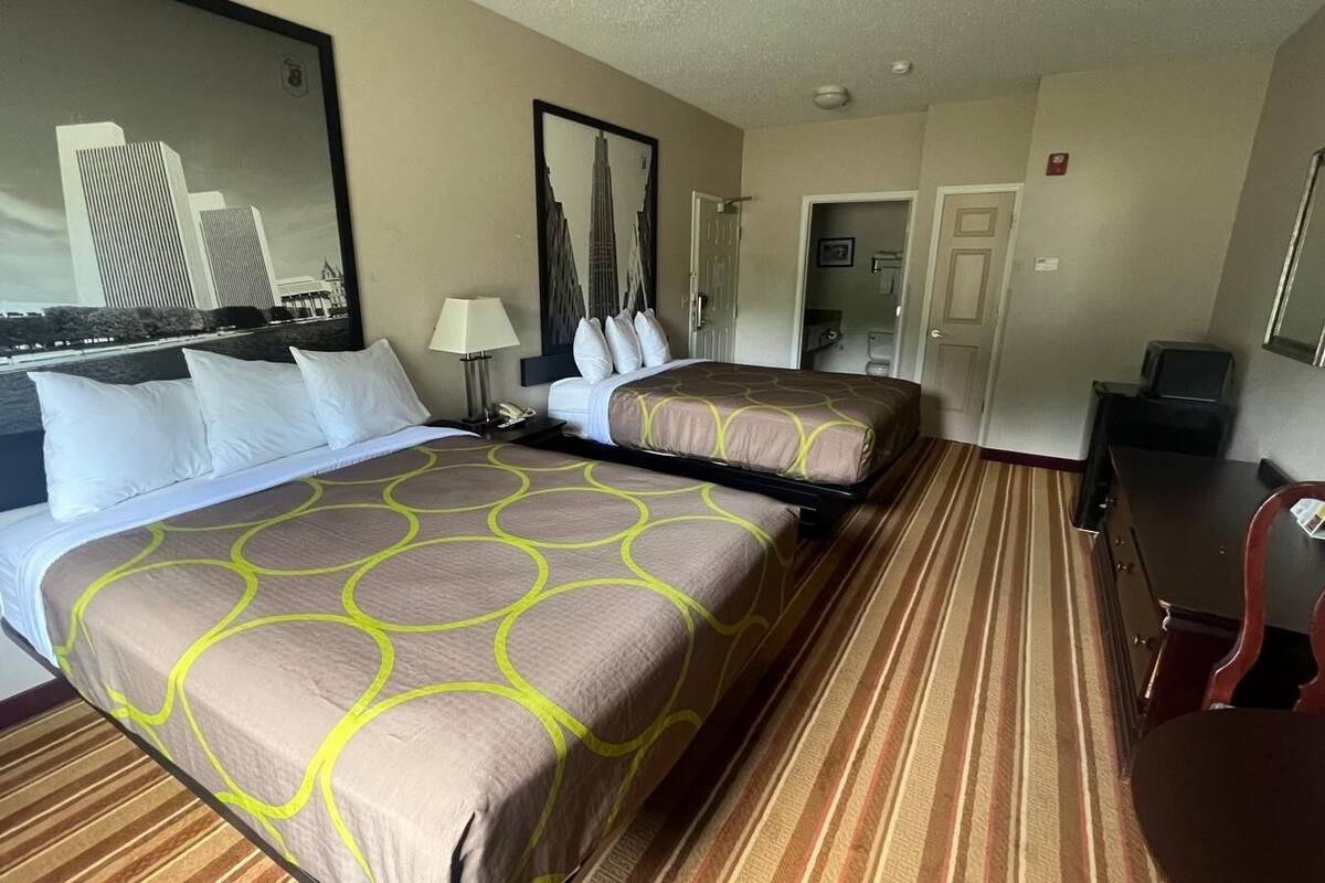 A hotel room with two beds, a desk, a chair, a lamp, and a large mirror.