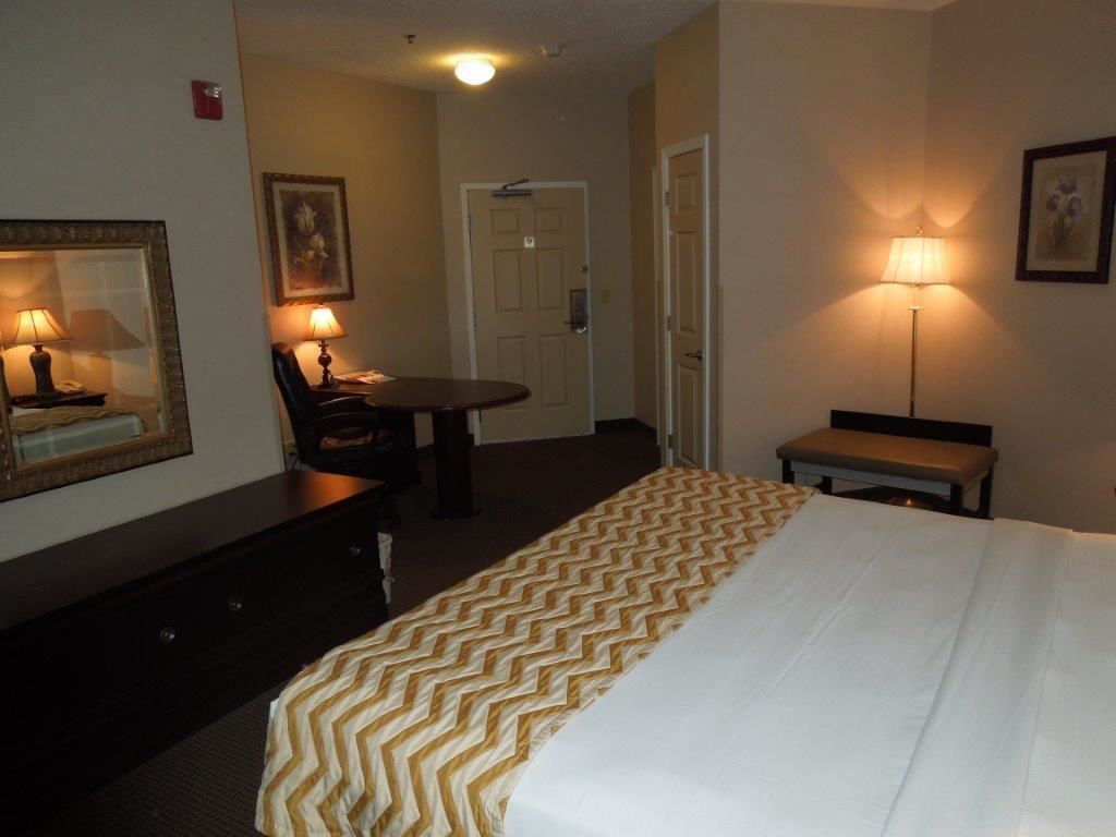 A hotel room with a bed, a desk, a chair, a lamp, and a door.