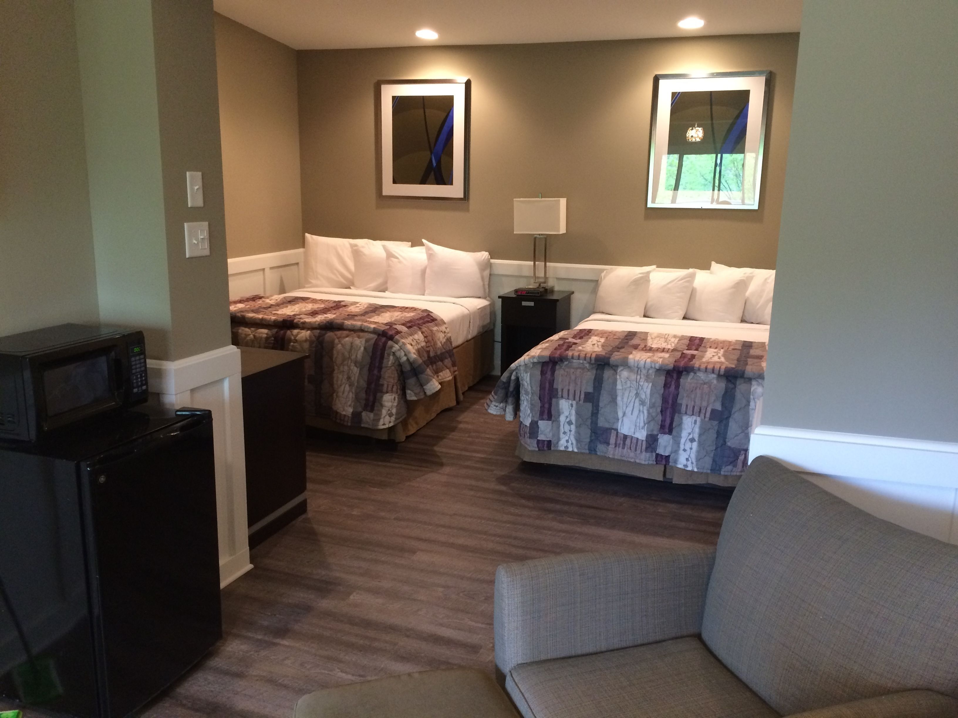 A hotel room with two beds, a desk with a microwave, a chair, and a nightstand with a lamp.