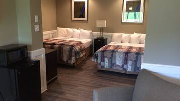 A hotel room with two beds, a desk with a microwave, a chair, and a nightstand with a lamp.