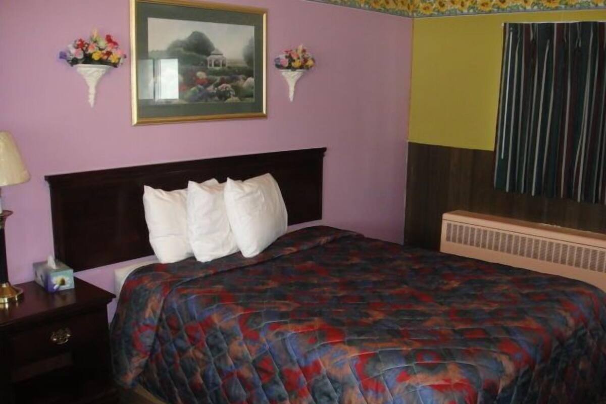A bedroom with a bed, a nightstand, a lamp, and two wall-mounted flower arrangements.