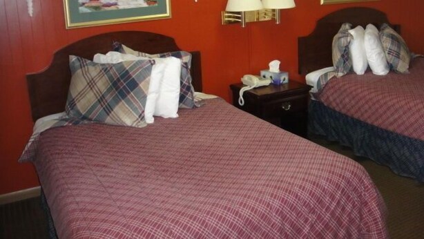 Habitación de hotel con dos camas, cada una con ropa de cama escocesa, una mesita de noche con teléfono y pañuelos, y lámparas fijadas a la pared.