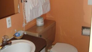 Un baño con una pared naranja, un lavabo blanco, un inodoro y un secador de pelo en la pared.