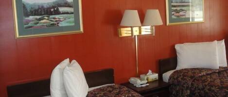 A hotel room with two beds, each with a floral-patterned bedspread, a nightstand with a lamp, and two framed landscape paintings on the walls.