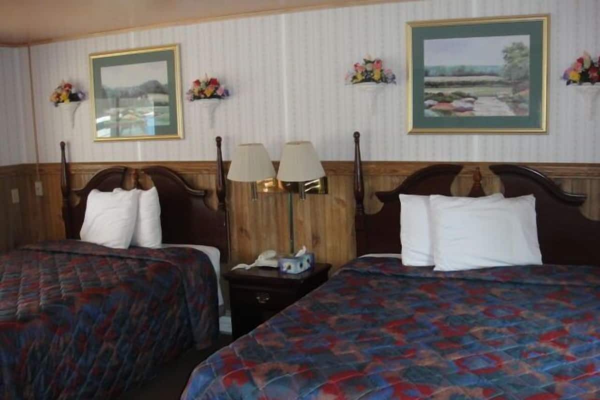 A hotel room with two beds, each with a patterned bedspread, a wooden headboard, and a nightstand with a lamp and a telephone.