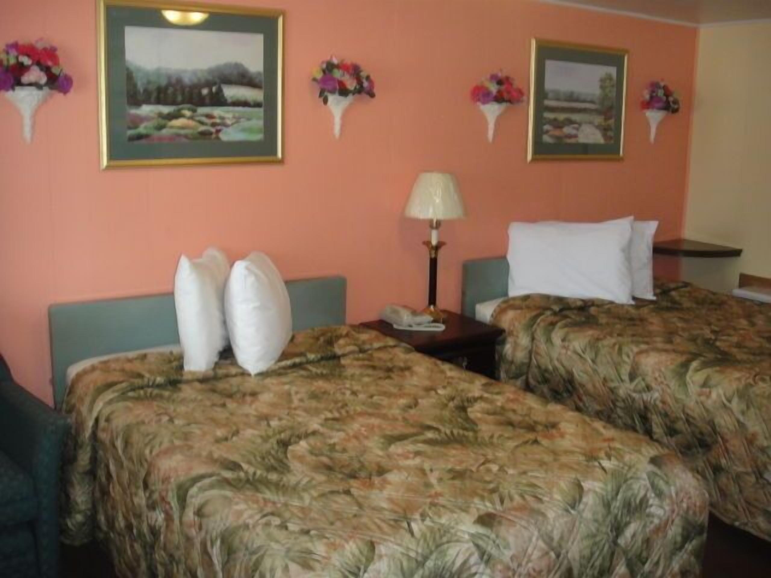 A hotel room with two beds, each with floral-patterned bedding, a nightstand with a lamp, and framed pictures on the wall.
