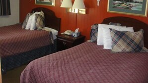 Una habitación de hotel con dos camas, cada una con una colcha y almohadas a cuadros. Hay dos lámparas de pared y dos cuadros enmarcados encima de las camas.