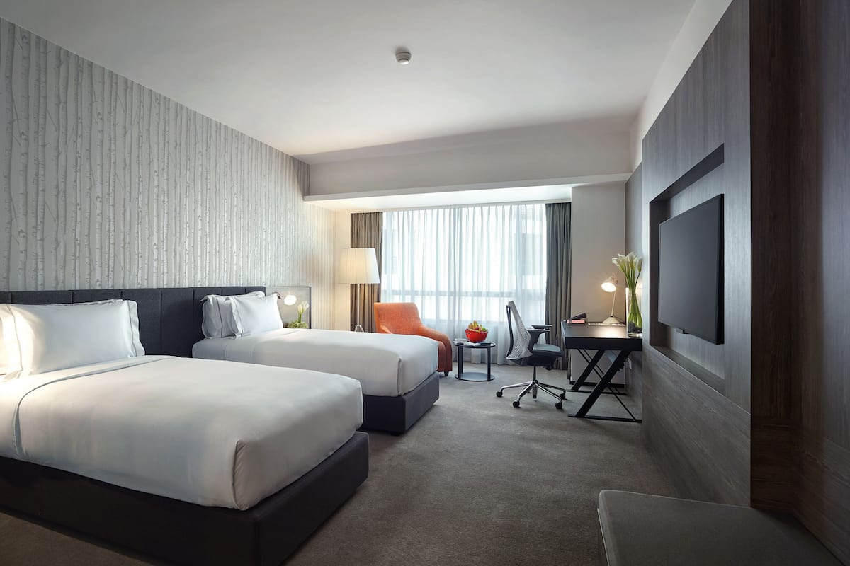Habitación de hotel con dos camas, un escritorio, una silla, un televisor y una ventana con cortinas.