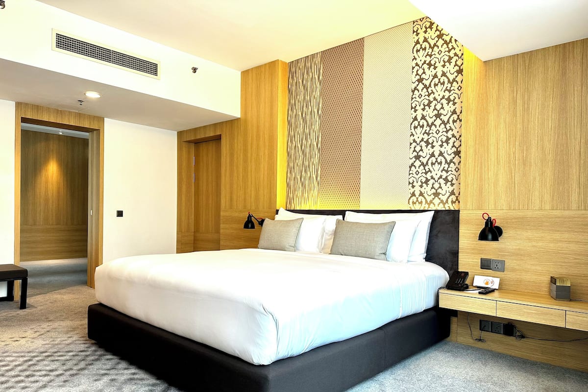 Una habitación de hotel moderna con una cama grande, cabecera de madera y una mesita de noche con lámpara.