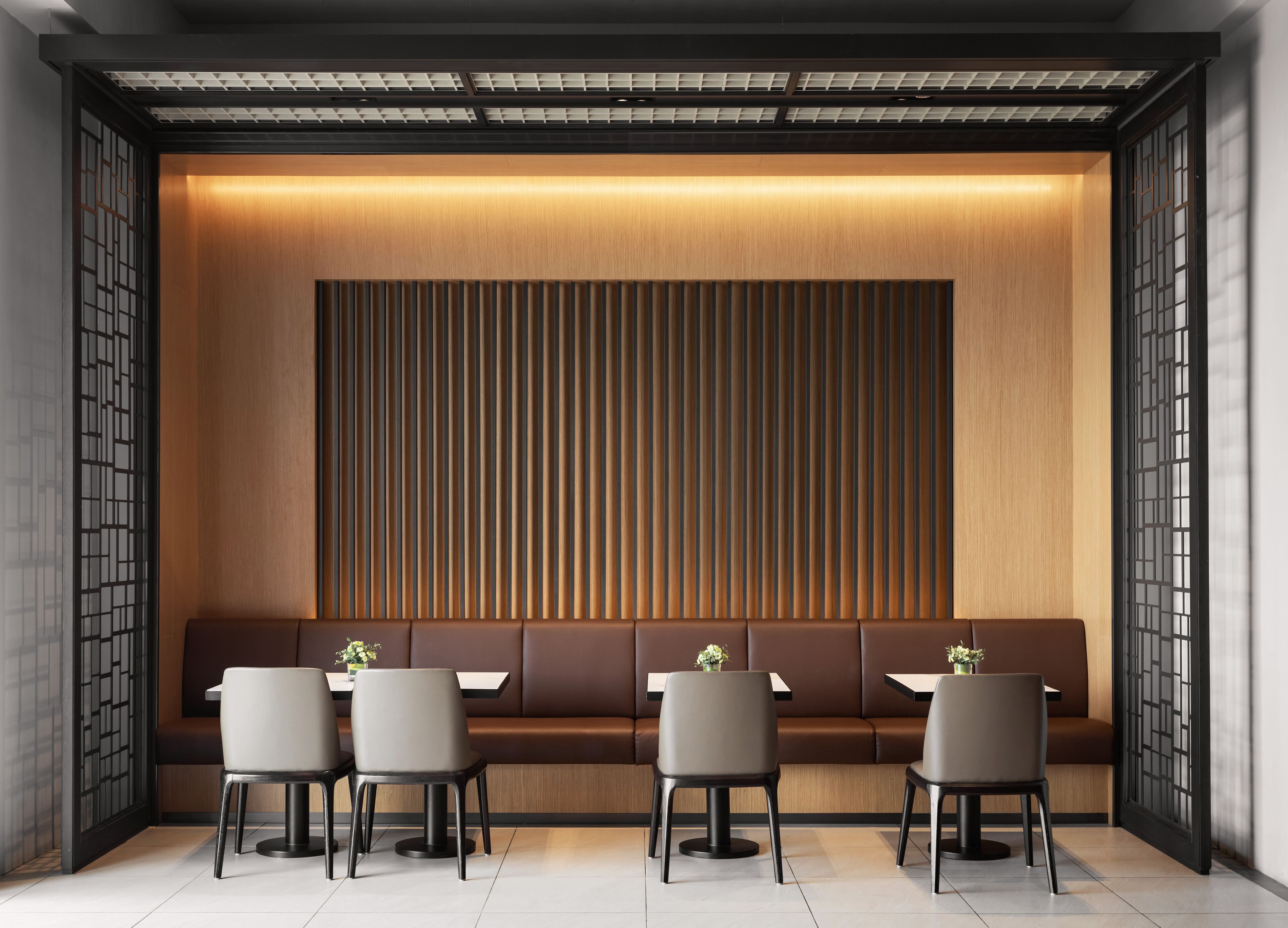 Un interior moderno con una larga banqueta, una mesa con sillas y un panel decorativo en la pared.