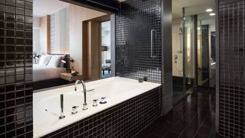 A modern bathroom with a large white bathtub, black tiled walls, and a glass shower enclosure.