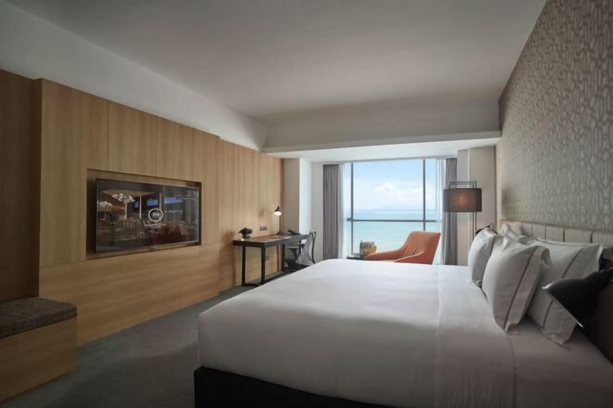 Une chambre d’hôtel moderne, dotée d’un grand lit, d’un petit bureau, d’une chaise et d’une grande fenêtre donnant sur la mer.
