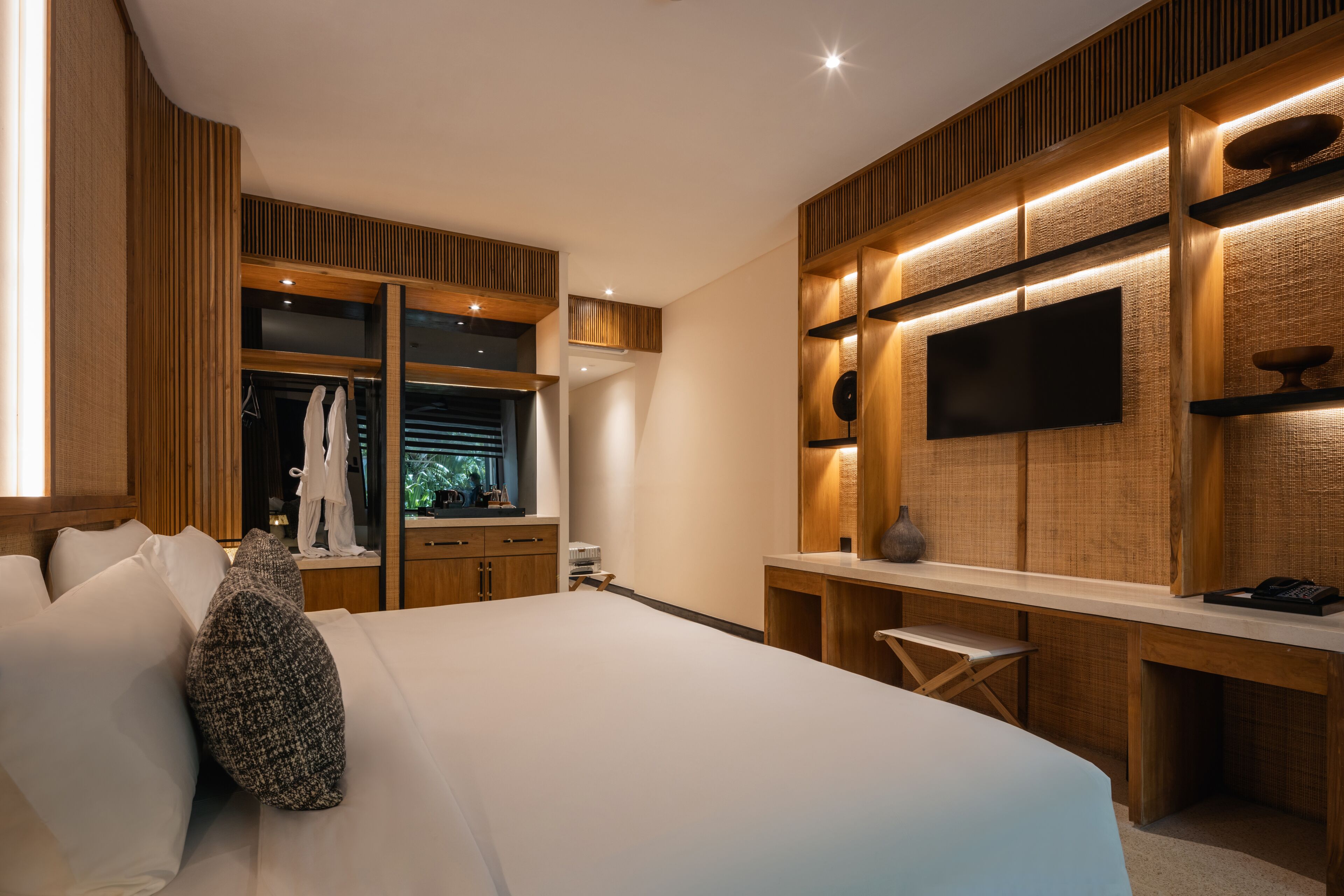Quarto moderno com uma cama grande, uma escrivaninha e uma TV fixada na parede.