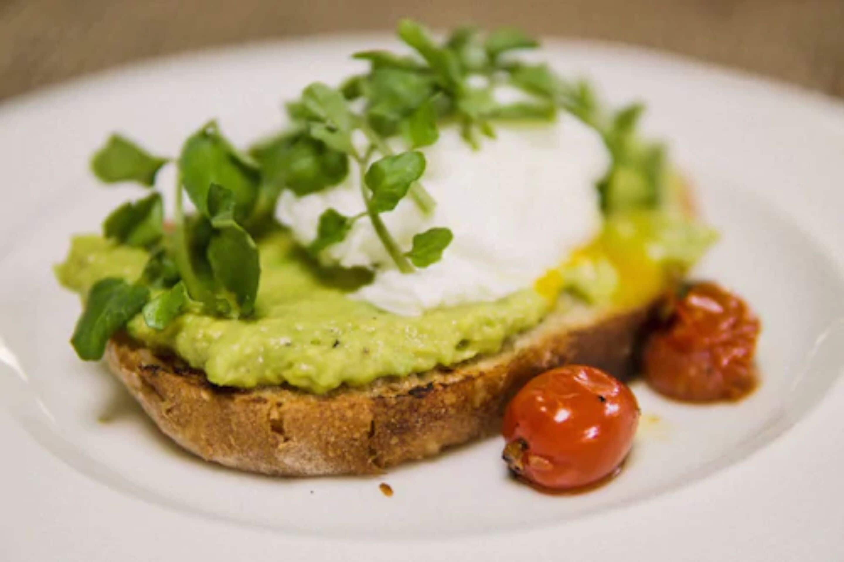 Ein Sandwich mit Avocado, Grünzeug und einem pochierten Ei auf einer Brotscheibe.
