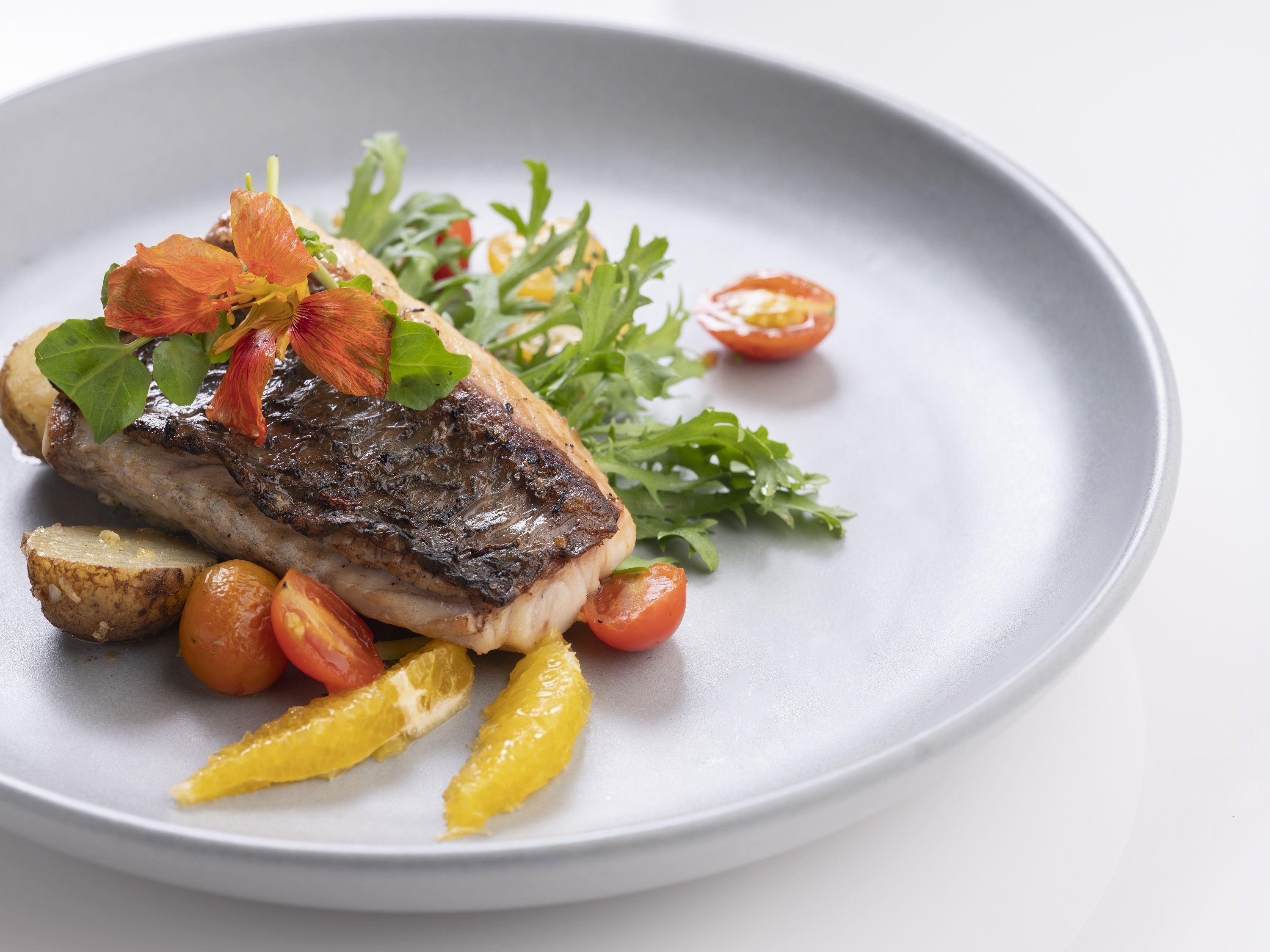 A plate with a grilled steak, roasted potatoes, cherry tomatoes, and lemon wedges.