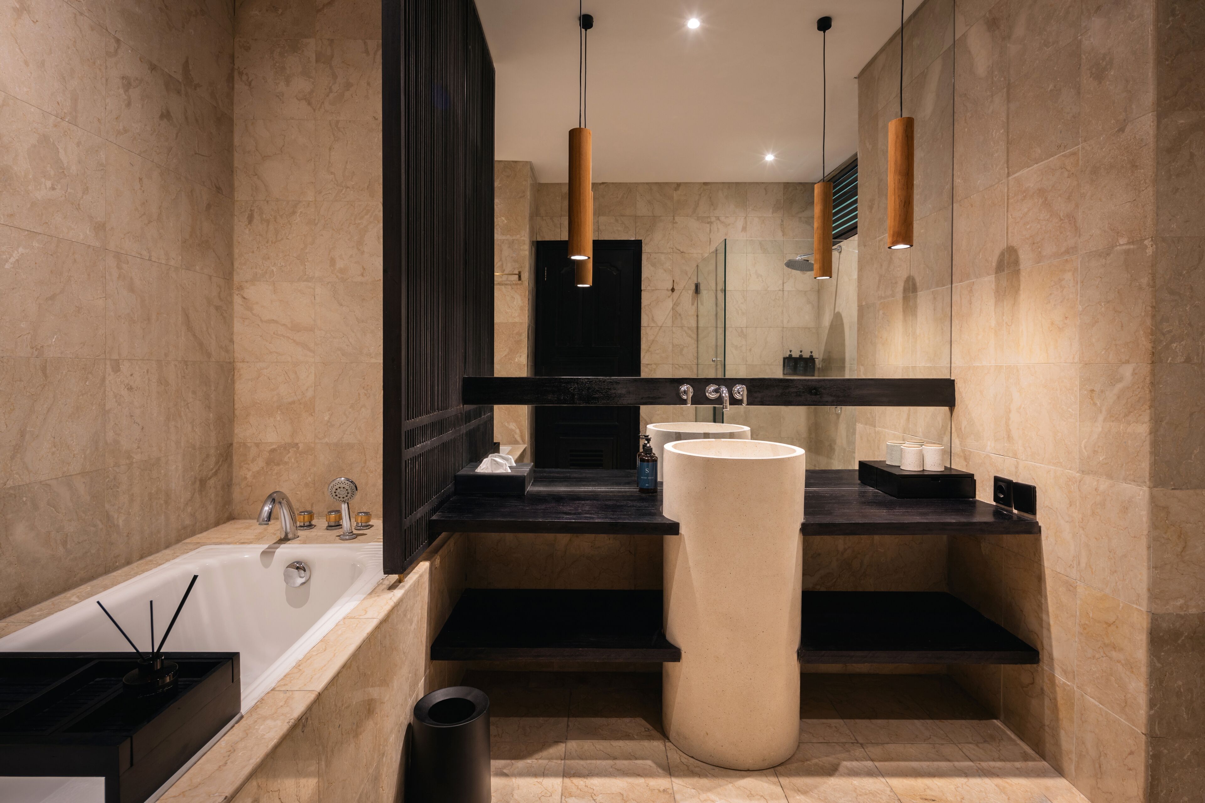 A modern bathroom with a large bathtub, a tall white column, and a black countertop with a sink and mirror.