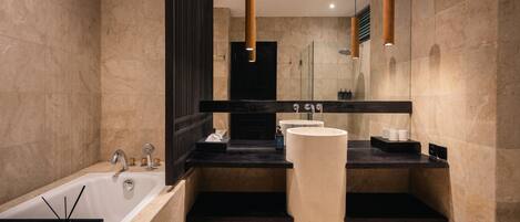 A modern bathroom with a large bathtub, a tall white column, and a black countertop with a sink and mirror.