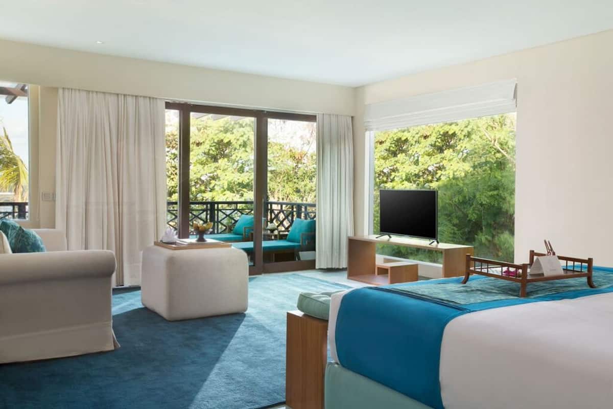 A hotel room with a large bed, a TV, a seating area with a view, and a balcony.