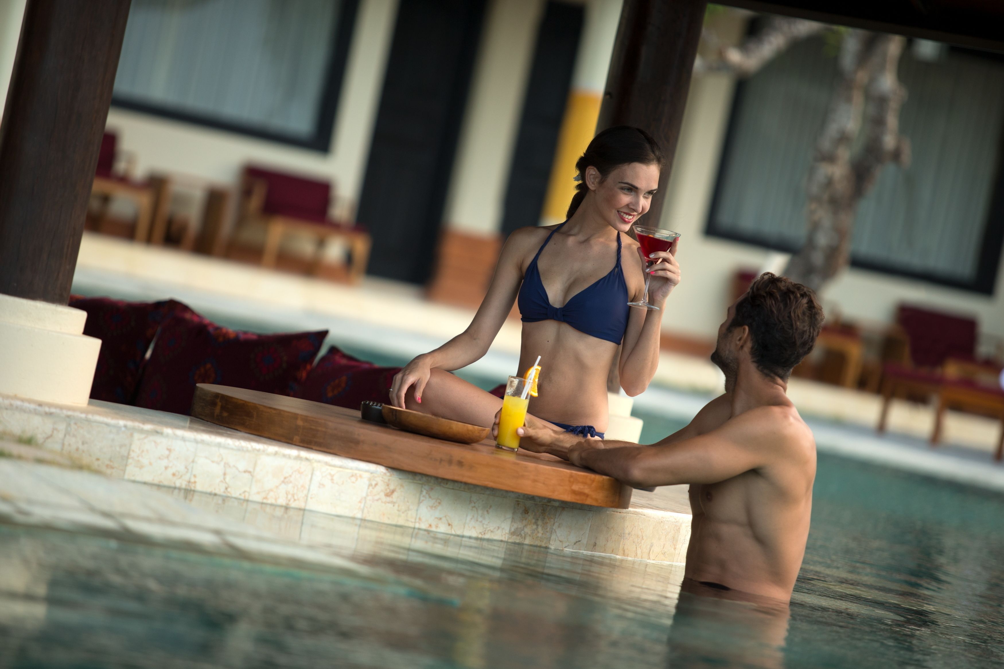 A poolside setting with a wooden deck, lounge chairs, and a glass of drink.