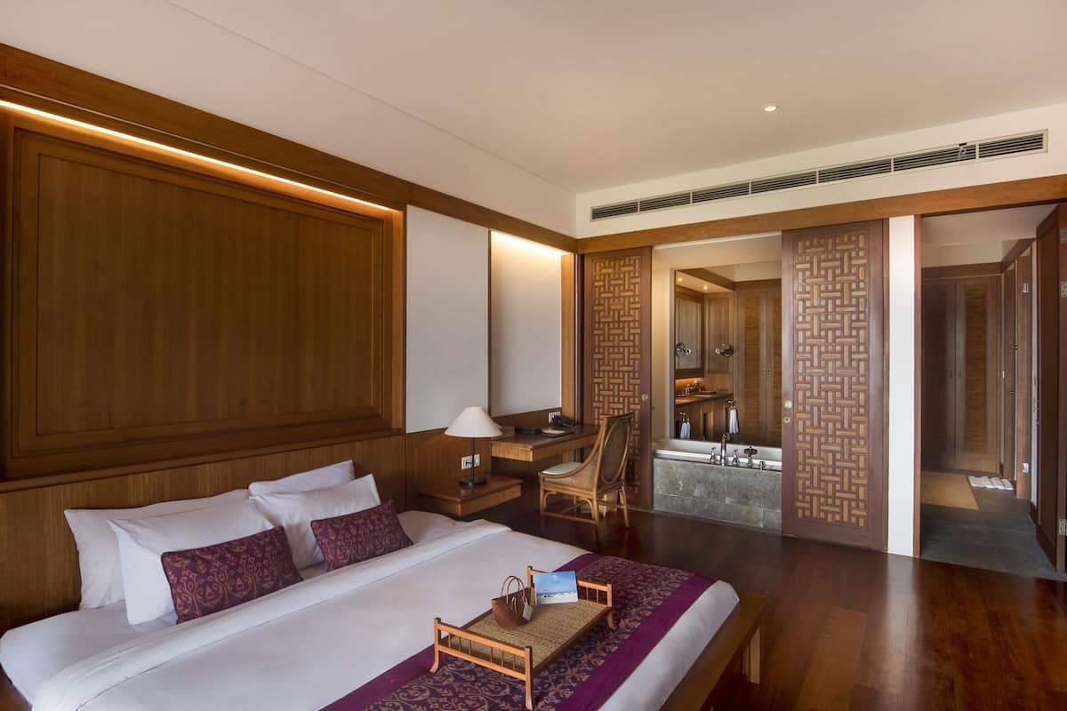 A hotel room with a large bed, a desk, a chair, a bathroom with a bathtub, and a wooden decorative wall.