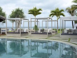 Zona junto a la piscina con mobiliario exterior bajo pérgolas, vista despejada del océano y una piscina bien cuidada.