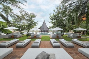 Un espace aménagé au bord de la piscine, avec des chaises longues et des parasols, un bâtiment central et une végétation luxuriante.