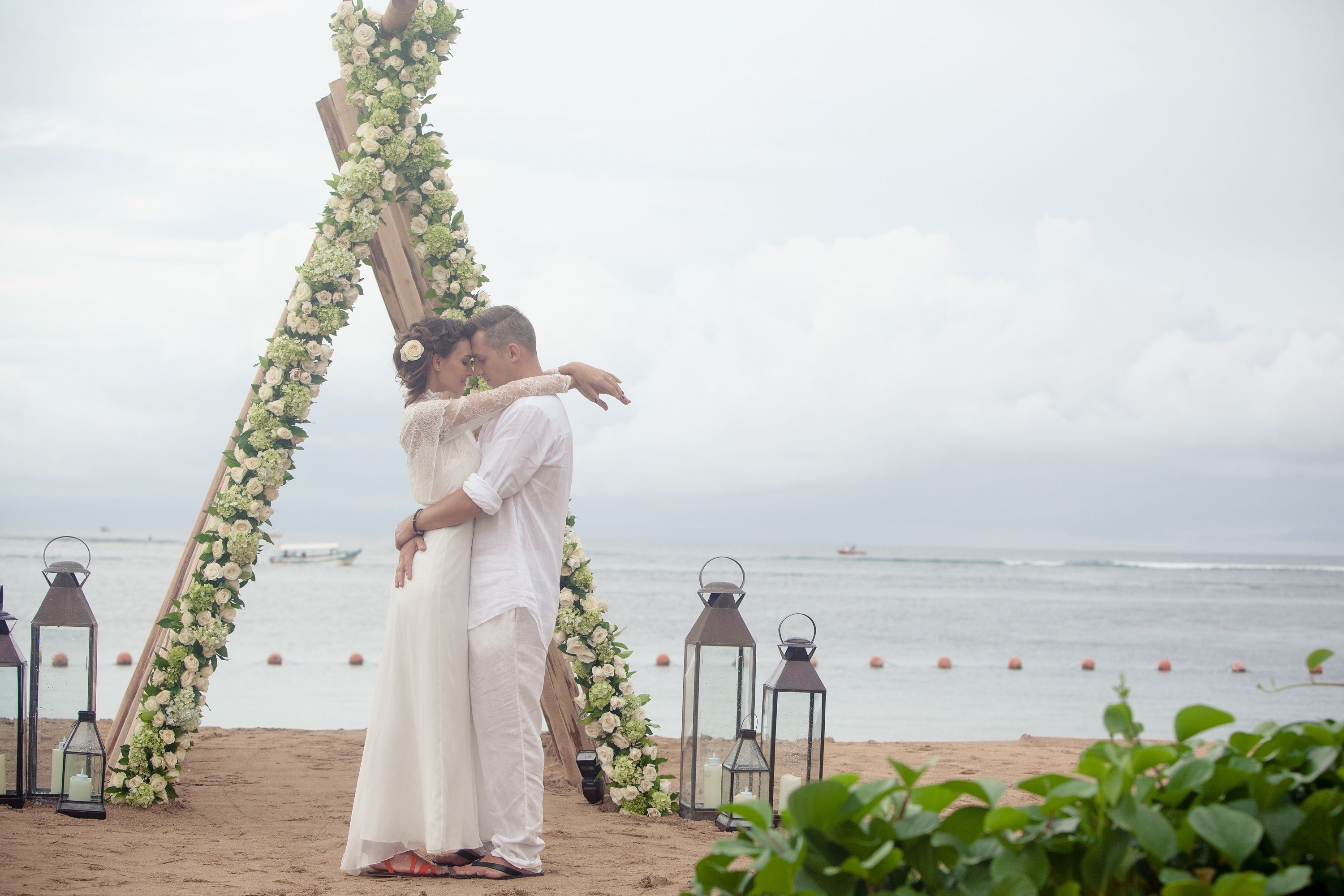 A beach wedding ceremony with a floral arch and lanterns.