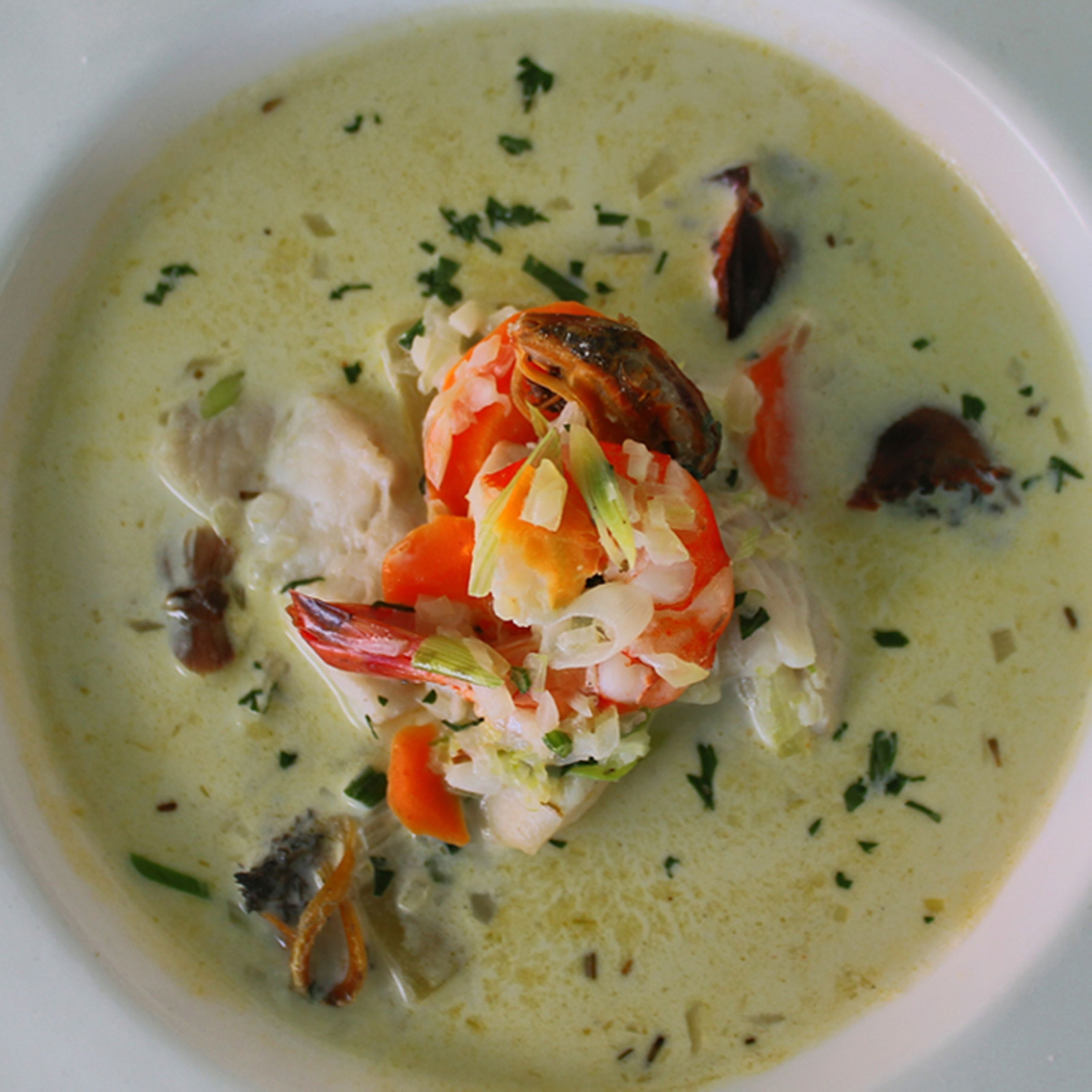Un bol de soupe de fruits de mer contenant des crevettes, des légumes et des herbes aromatiques.
