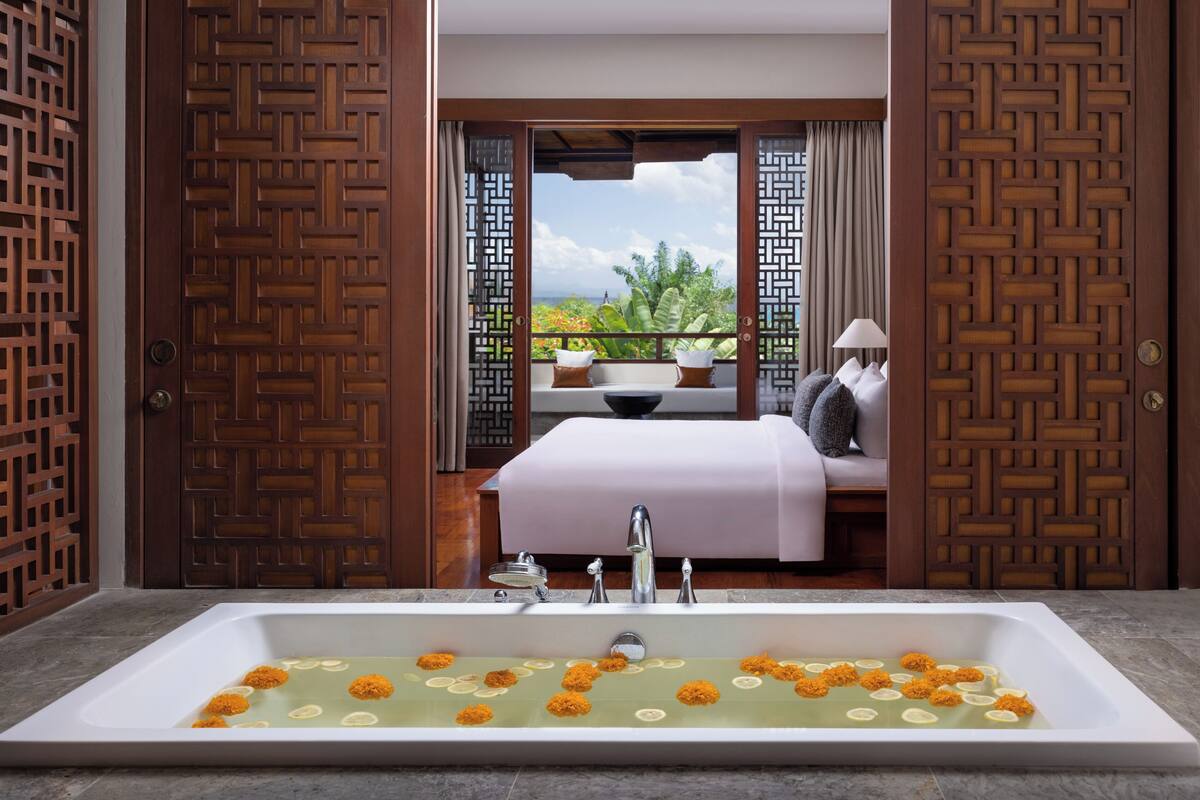A bathroom with a large bathtub, a bed with a view, and a wooden door with intricate patterns.