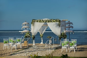 A beach wedding setup with a white arch and chairs, overlooking the ocean.