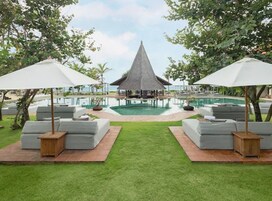 Un área junto a la piscina con sillones de descanso y sombrillas, una estructura de techo de paja y una vista despejada de la piscina.