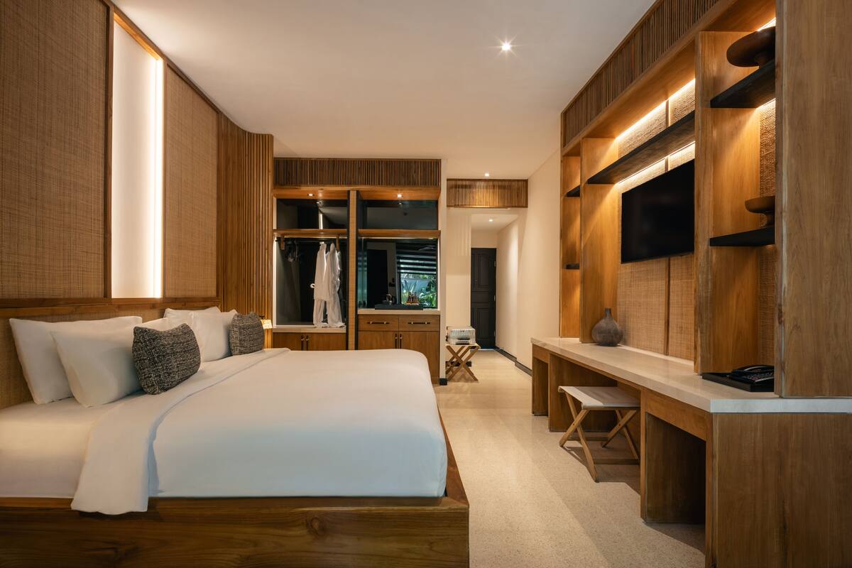 A modern bedroom with a large bed, wooden shelving, a desk, and a television.