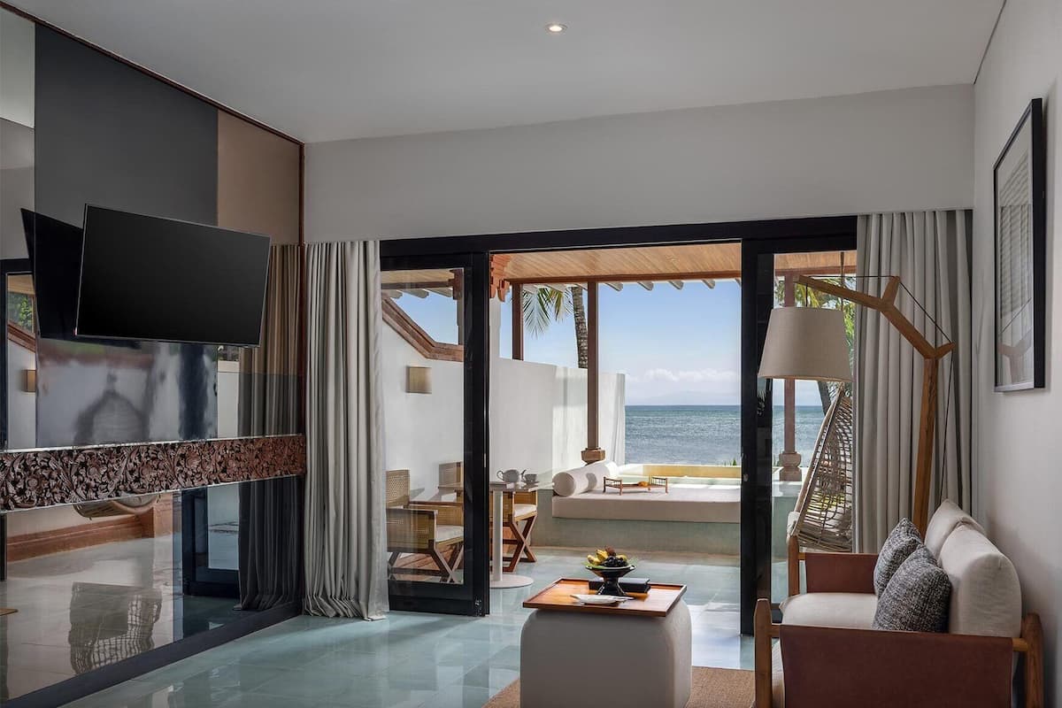 A modern hotel room with a large TV, a dining area with a table and chairs, and a view of the ocean.