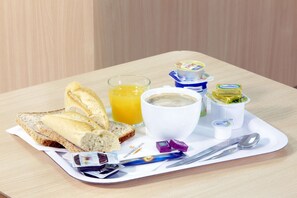 Ein Frühstücksbrett mit Toast, Orangensaft, Kaffee, Butter, Marmelade und einer Zeitung.