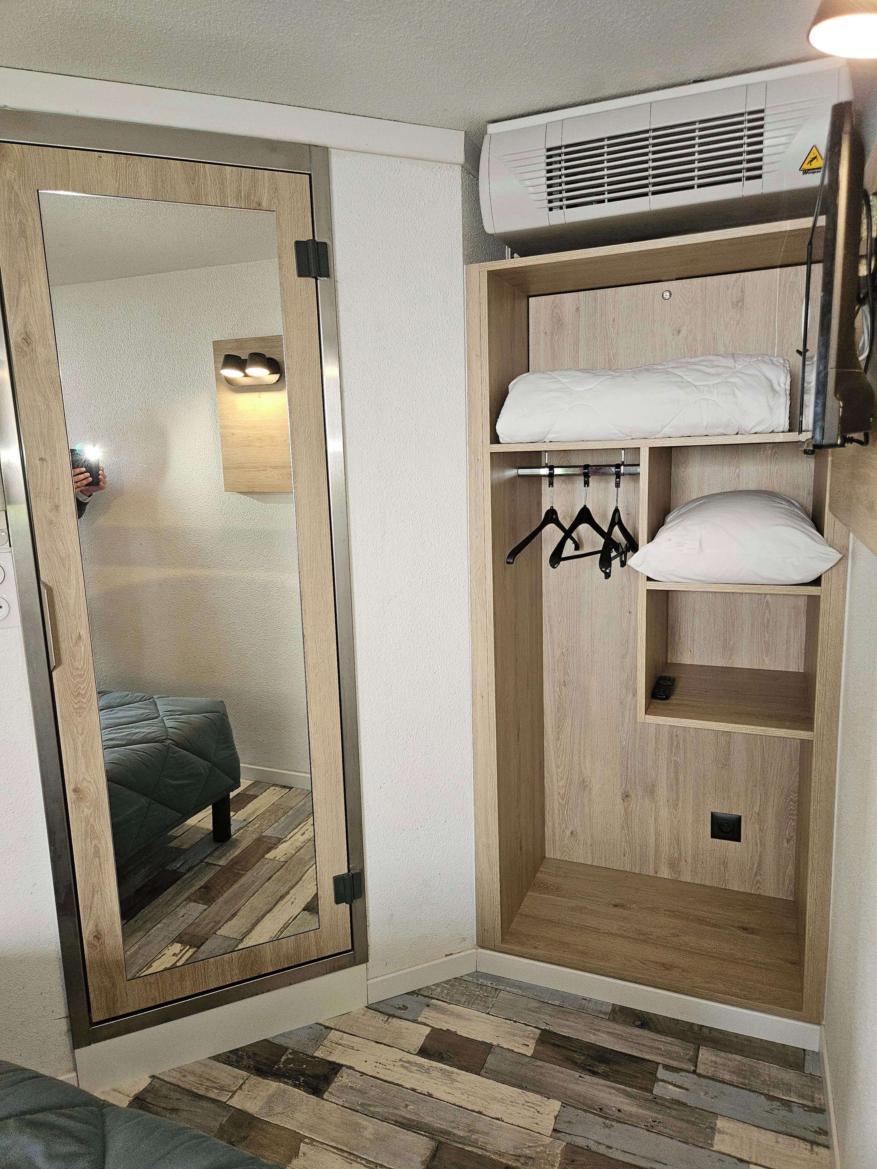 A compact room with a mirrored closet door, a bunk bed, a hanging rack, and a built-in air conditioning unit.