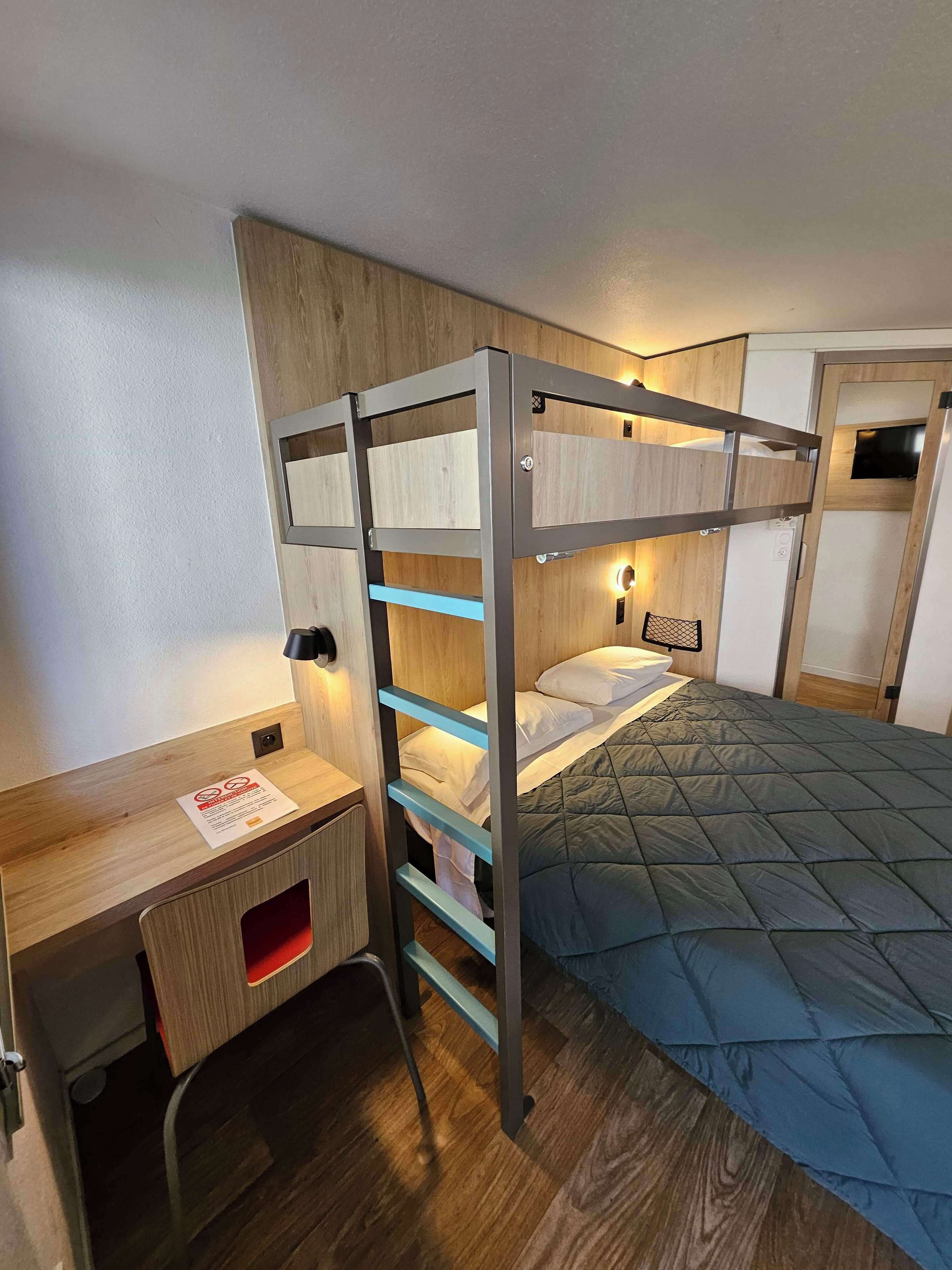 A bunk bed with a desk and a bed, wooden walls, and a small TV.
