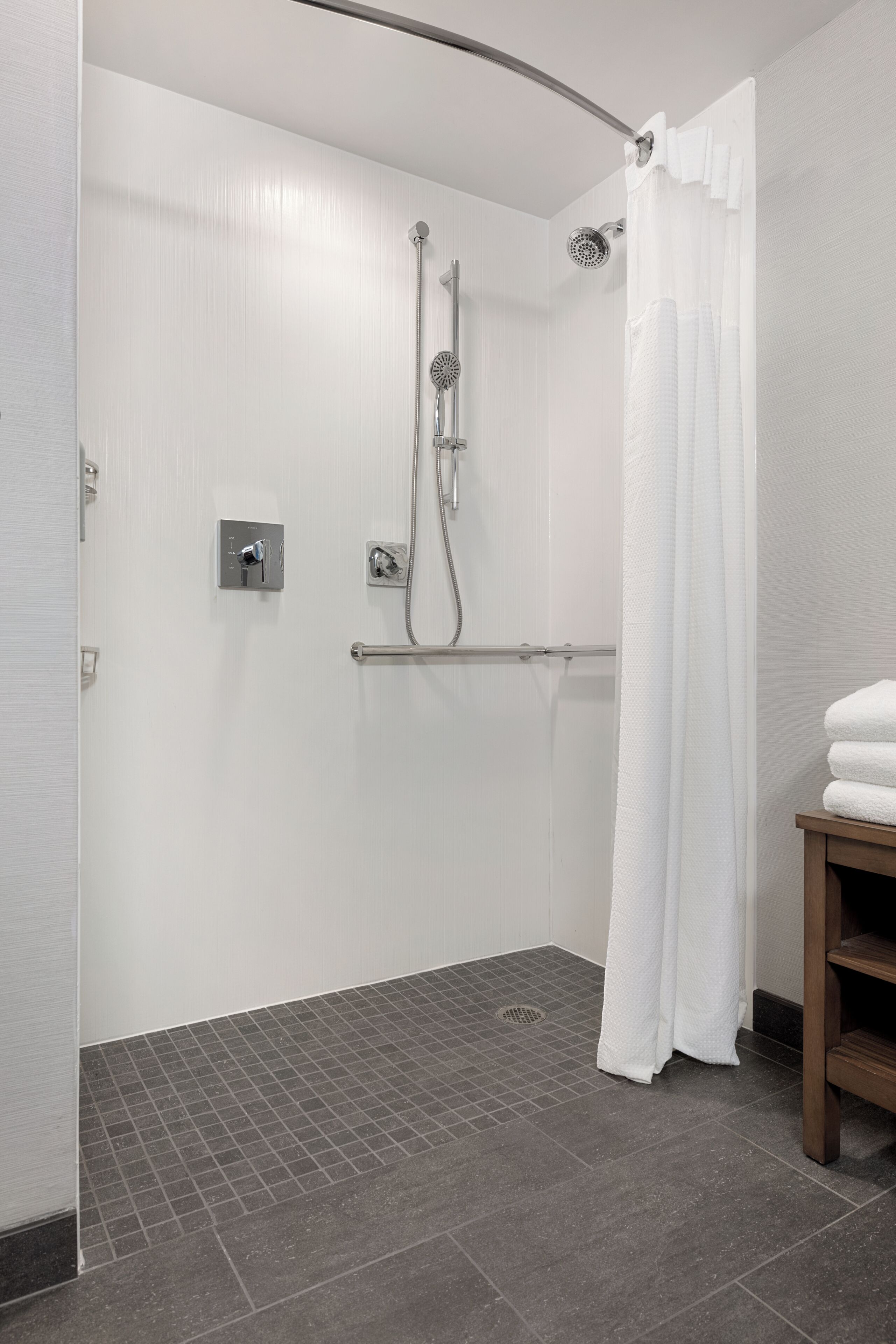 A modern shower with a curved showerhead, a towel rack, and a white shower curtain.