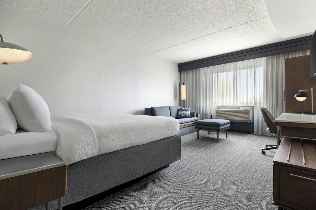 A modern hotel room with a large bed, a desk, a chair, and a sofa.