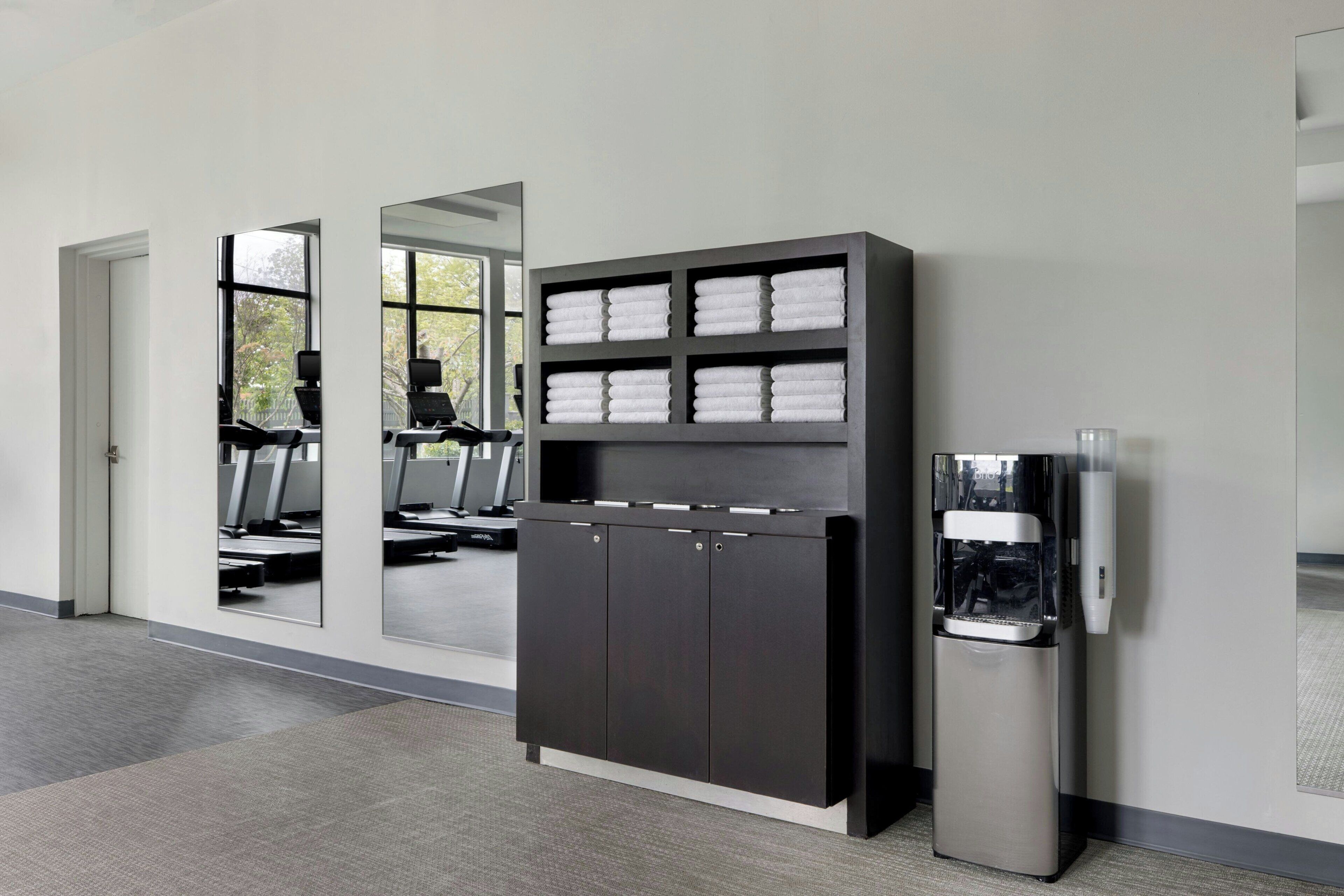 A modern hotel lobby with a mirrored wall, a water dispenser, and a seating area with exercise equipment.