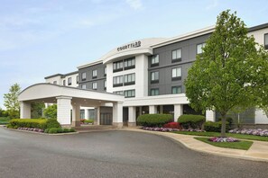 A Courtyard hotel with a modern design, featuring a covered entrance, multiple floors, and landscaped gardens. - Courtyard by Marriott Republic Aprt Long Island/Farmingdale (Farmingdale)
