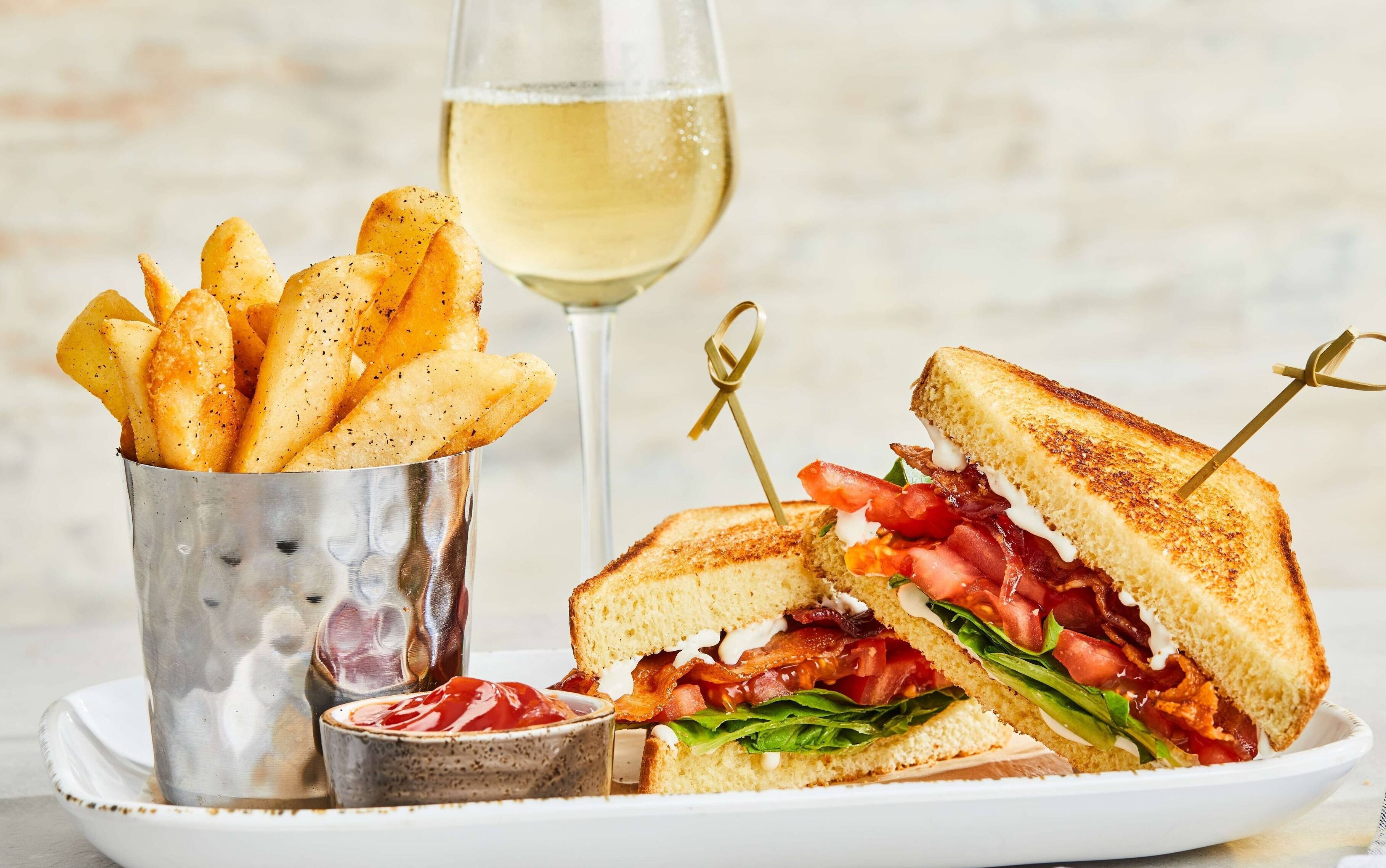Une assiette avec un sandwich grillé, une portion de frites et un verre de vin blanc.