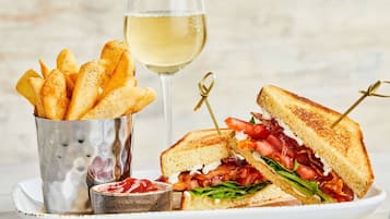 Une assiette avec un sandwich grillé, une portion de frites et un verre de vin blanc.